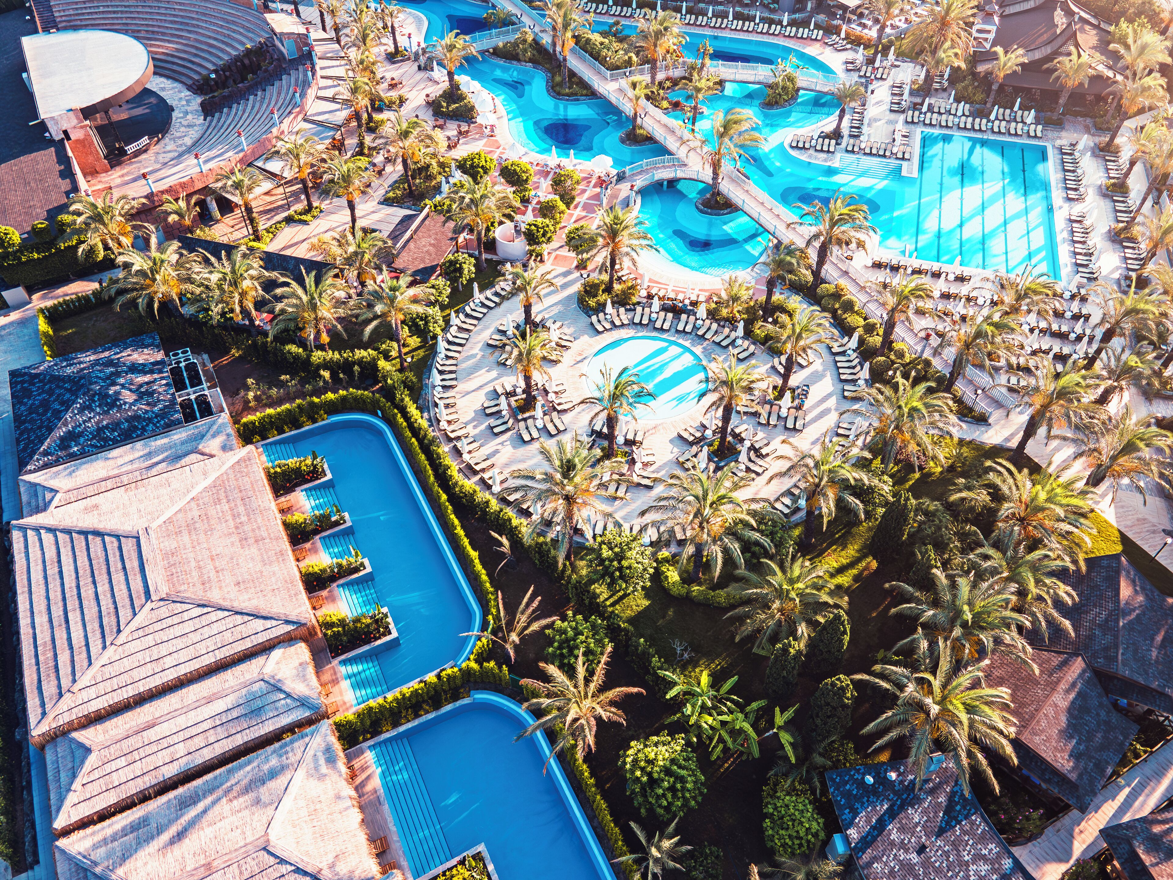 An aerial view of a resort with multiple swimming pools, palm trees, and sun loungers.