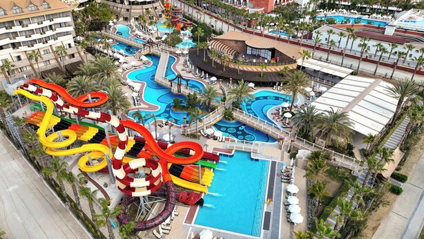 An aerial view of a resort with multiple swimming pools, water slides, and lounge areas surrounded by palm trees. - Royal Dragon Hotel – All Inclusive (Manavgat)