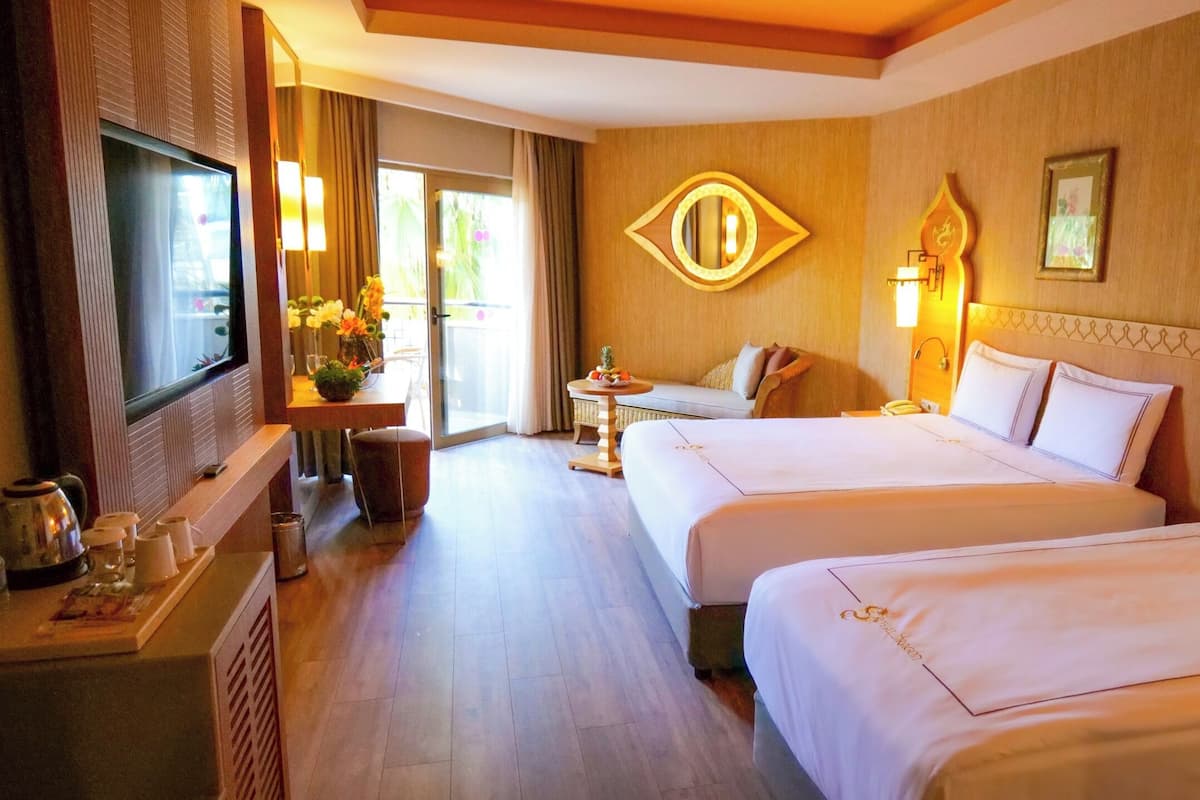 A hotel room with two beds, a TV, a small table with a vase of flowers, and a balcony with curtains.