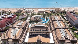 A resort with a large swimming pool, multiple buildings with traditional architecture, and a beach in the background. - Royal Dragon Hotel – All Inclusive (Manavgat)