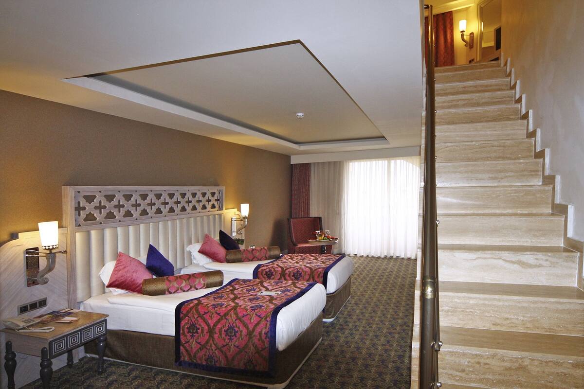 A hotel room with two beds, a desk, a chair, and a staircase.
