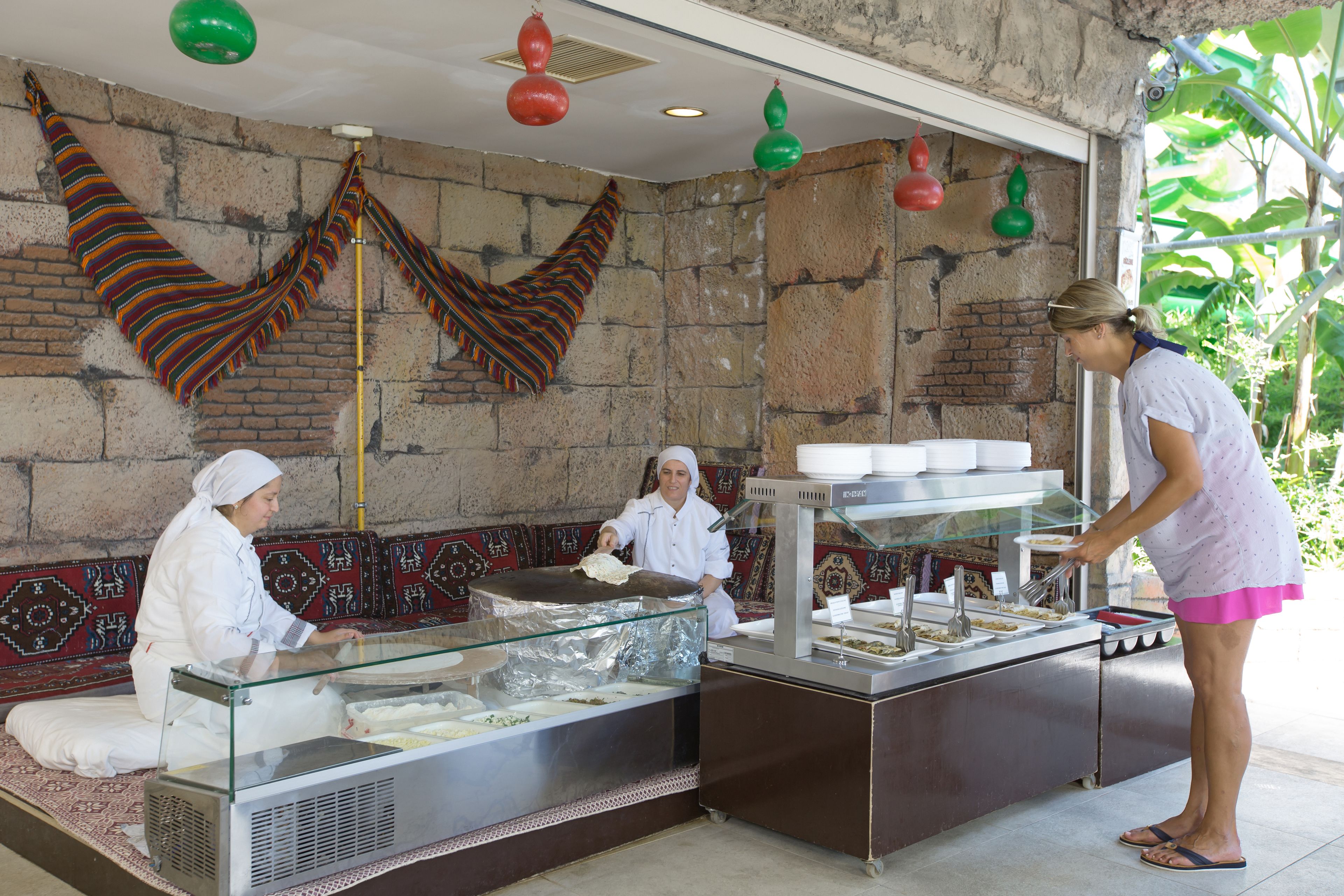 A buffet setup with a glass display case, a seating area with patterned cushions, and a brick wall.