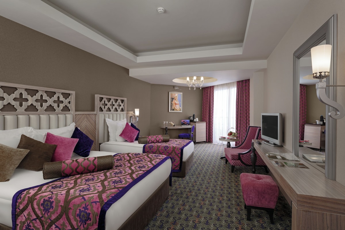 A hotel room with two beds, a desk with a computer, a TV, and a mirror.