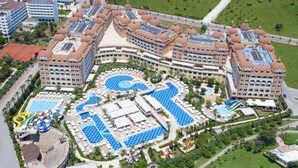 An aerial view of a resort with multiple swimming pools, a beach area with sun loungers, and a large building with a dome roof. - Royal Alhambra Palace – All Inclusive (Manavgat)