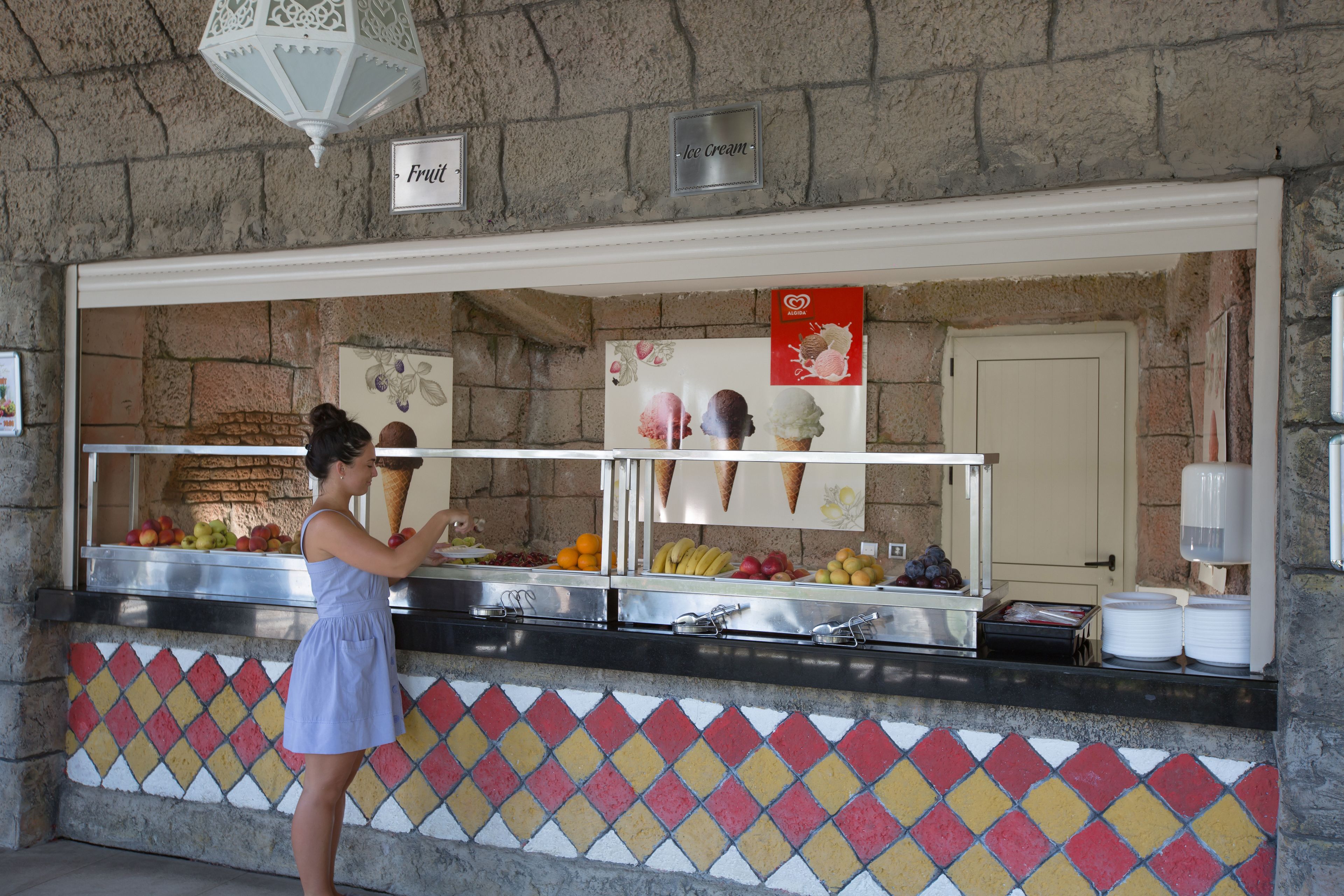 Un espacio de comida con una pared de piedra, una exhibición de frutas y un letrero de helados.