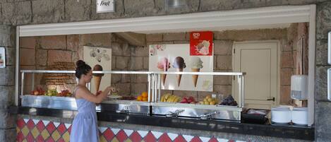Un espacio de comida con una pared de piedra, una exhibición de frutas y un letrero de helados.