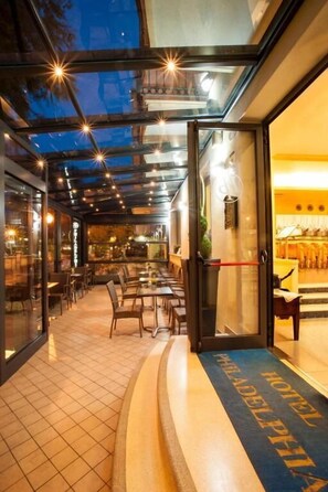 A hotel lobby with a glass ceiling, a reception desk, and a seating area with tables and chairs. - Philadelphia (Cattolica)
