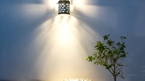 Un área de estar moderna al aire libre con una lámpara de pared, un árbol pequeño y cojines estampados.