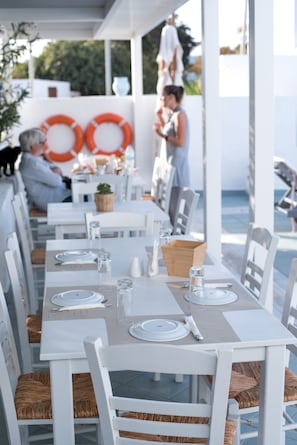 Un restaurante frente al mar con mesas blancas y sillas de mimbre, que ofrece una vista despejada del océano.