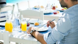 Una mesa de comedor con alimentos para el desayuno, como jugo de naranja, una jarrón y un bol de fruta.