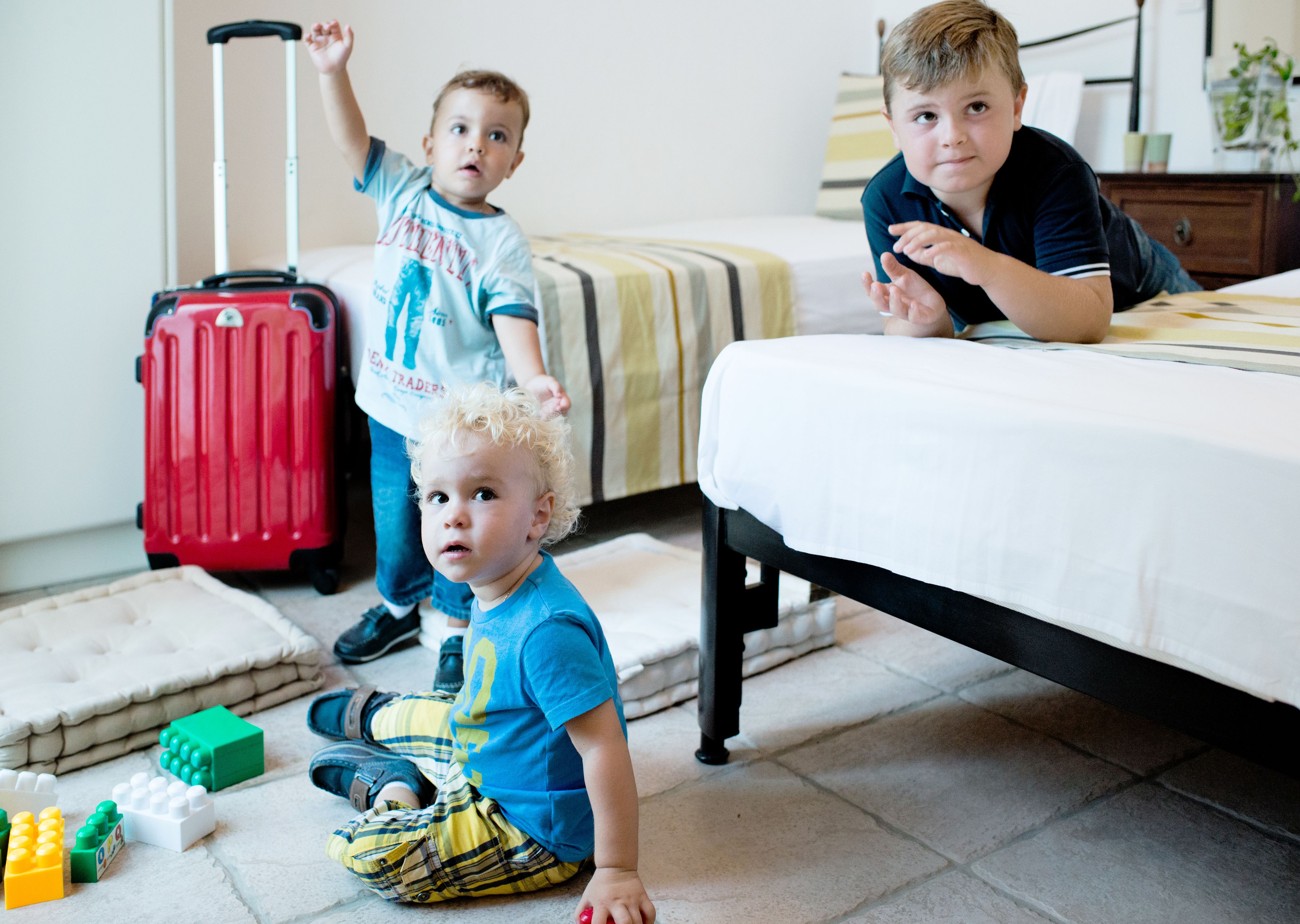 A hotel room with a bed, a suitcase, and children's toys on the floor.