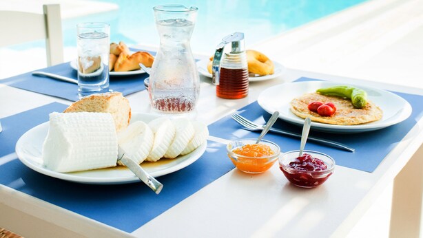 Una mesa de comedor con productos para el desayuno y vistas a una piscina y montañas.
