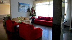 Een woonkamer met een rode bank, een beige bank en een rode fauteuil. Er staat een kerstboom en hangt een schilderij aan de muur.