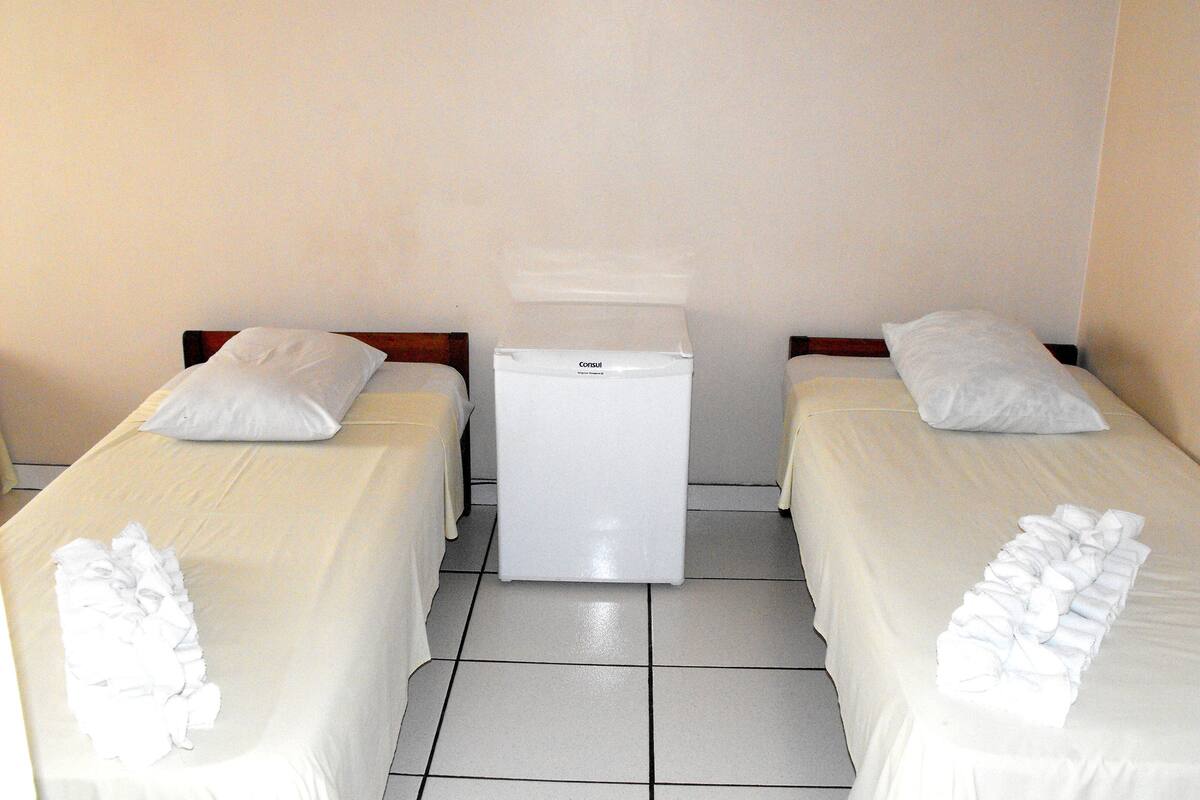 Ett hotellrum med två separata sängar, ett litet vitt kylskåp och ett klinkergolv.