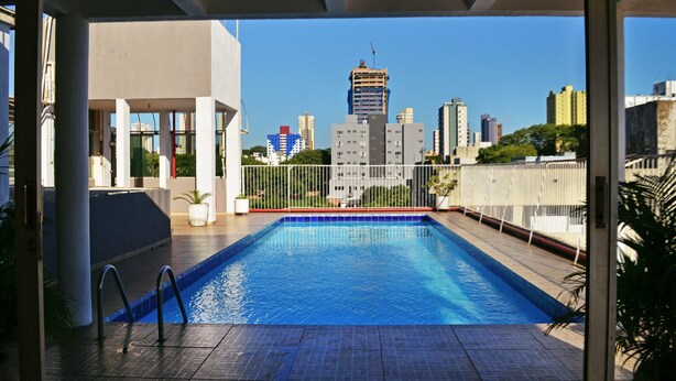 Een buitenzwembad met uitzicht op een stadshemelbeeld, omgeven door een hek en potplanten.