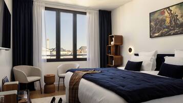 Habitación de hotel con una cama grande, una silla, un escritorio y vistas a la ciudad desde la ventana.