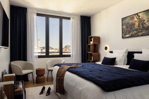 Habitación de hotel con una cama grande, una silla, un escritorio y vistas a la ciudad desde la ventana.