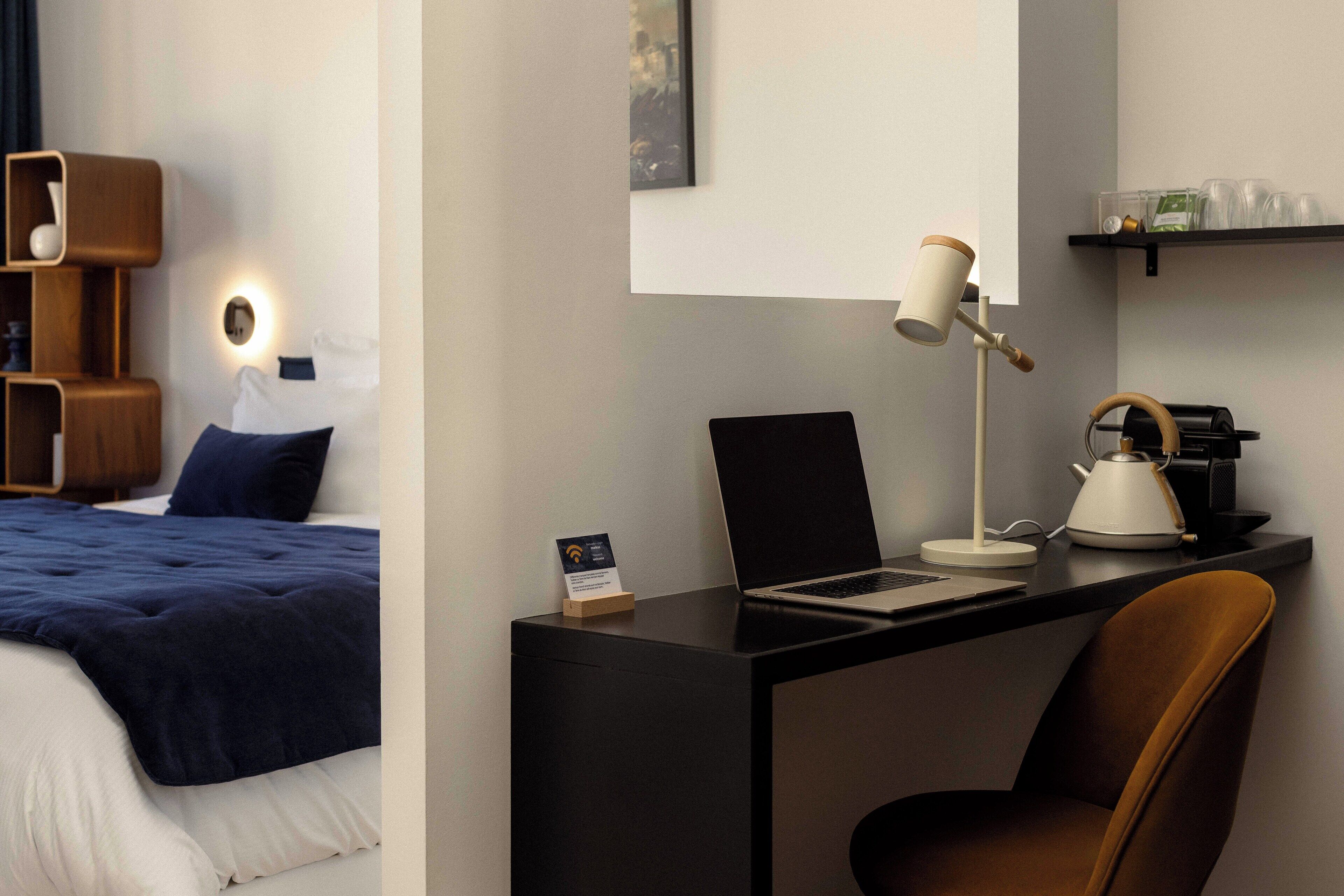 Hotelkamer met een bed, een bureau met een laptop, een stoel, een koffiezetapparaat en een plank met glazen.