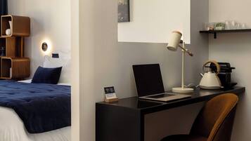 Hotelkamer met een bed, een bureau met een laptop, een stoel, een koffiezetapparaat en een plank met glazen.