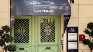A building with a green door, a black awning with the name "Markus," and a balcony with chairs. - Markus (Angers)