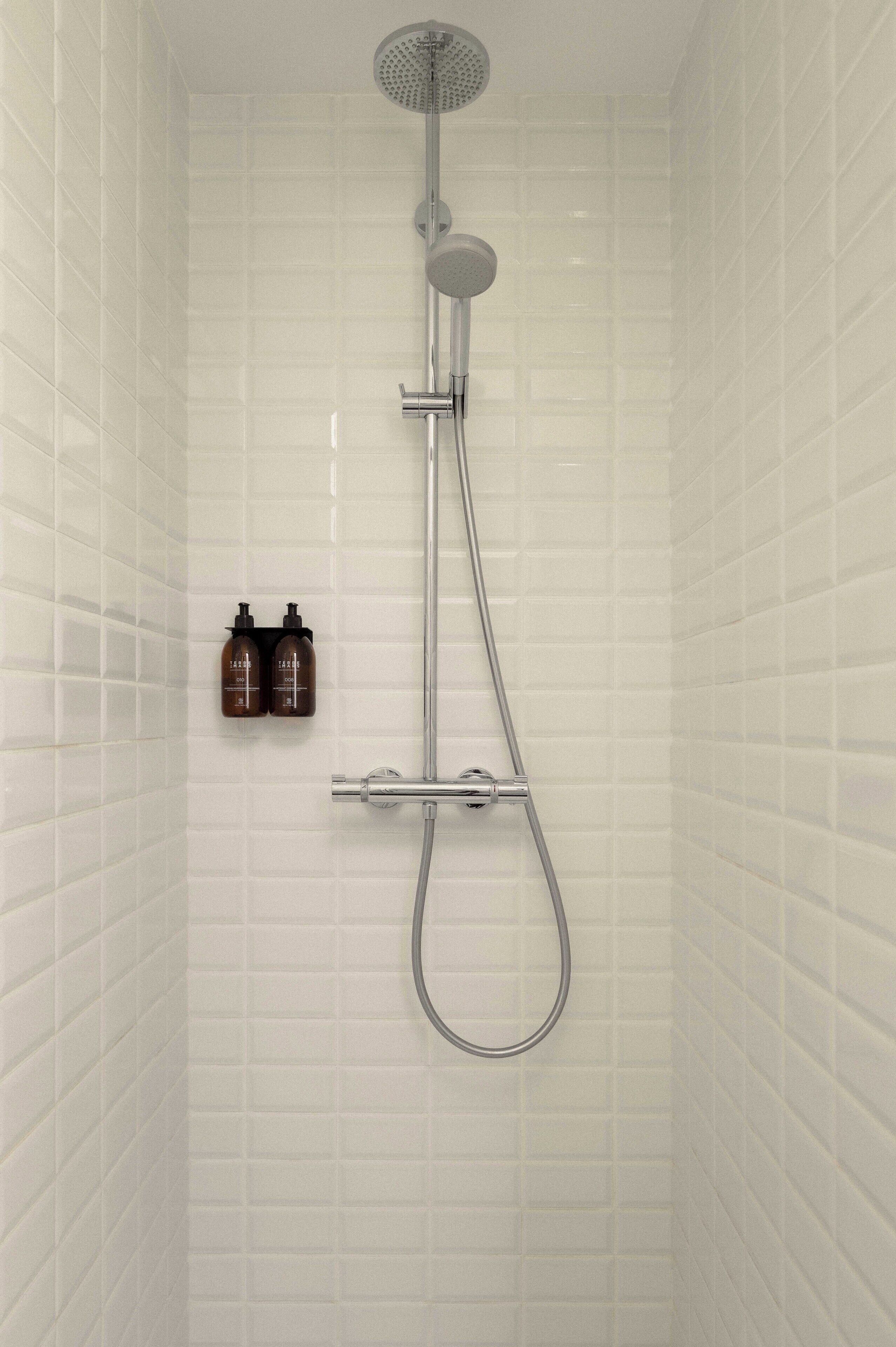 Ducha con cabezal de ducha de mano y grifo empotrado en la pared, con dos botellas de champú colgadas.