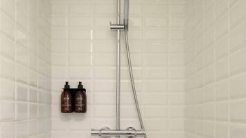 Ducha con cabezal de ducha de mano y grifo empotrado en la pared, con dos botellas de champú colgadas.