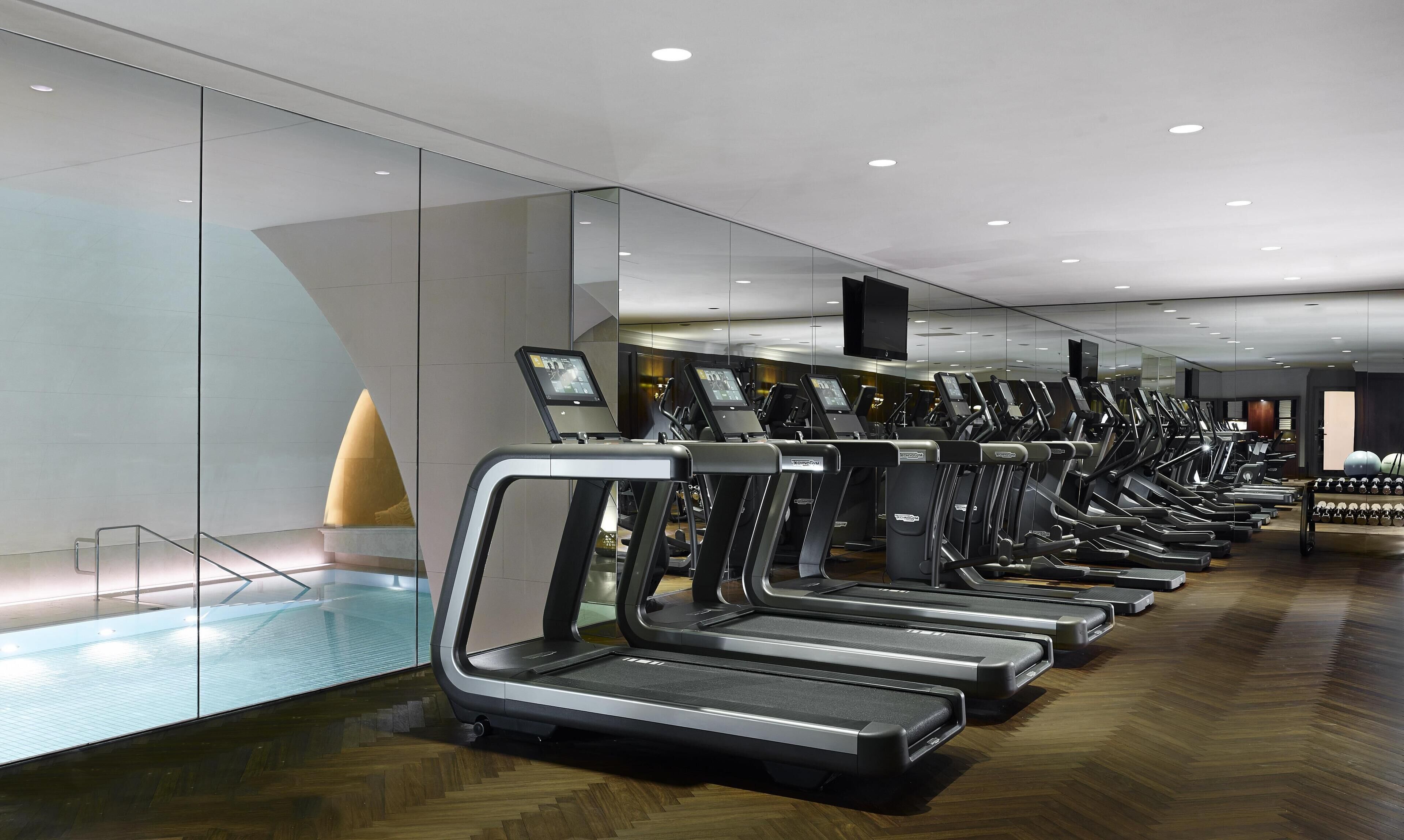 Un gimnasio moderno con cintas de correr, un muro de cristal y suelo de madera.