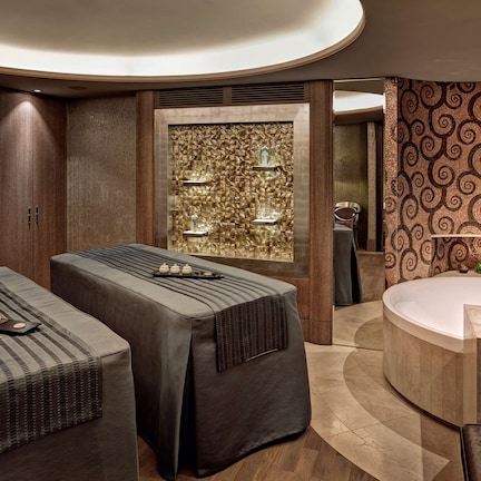 A spa room with two massage tables, a large bathtub, and a decorative wall with a patterned design.