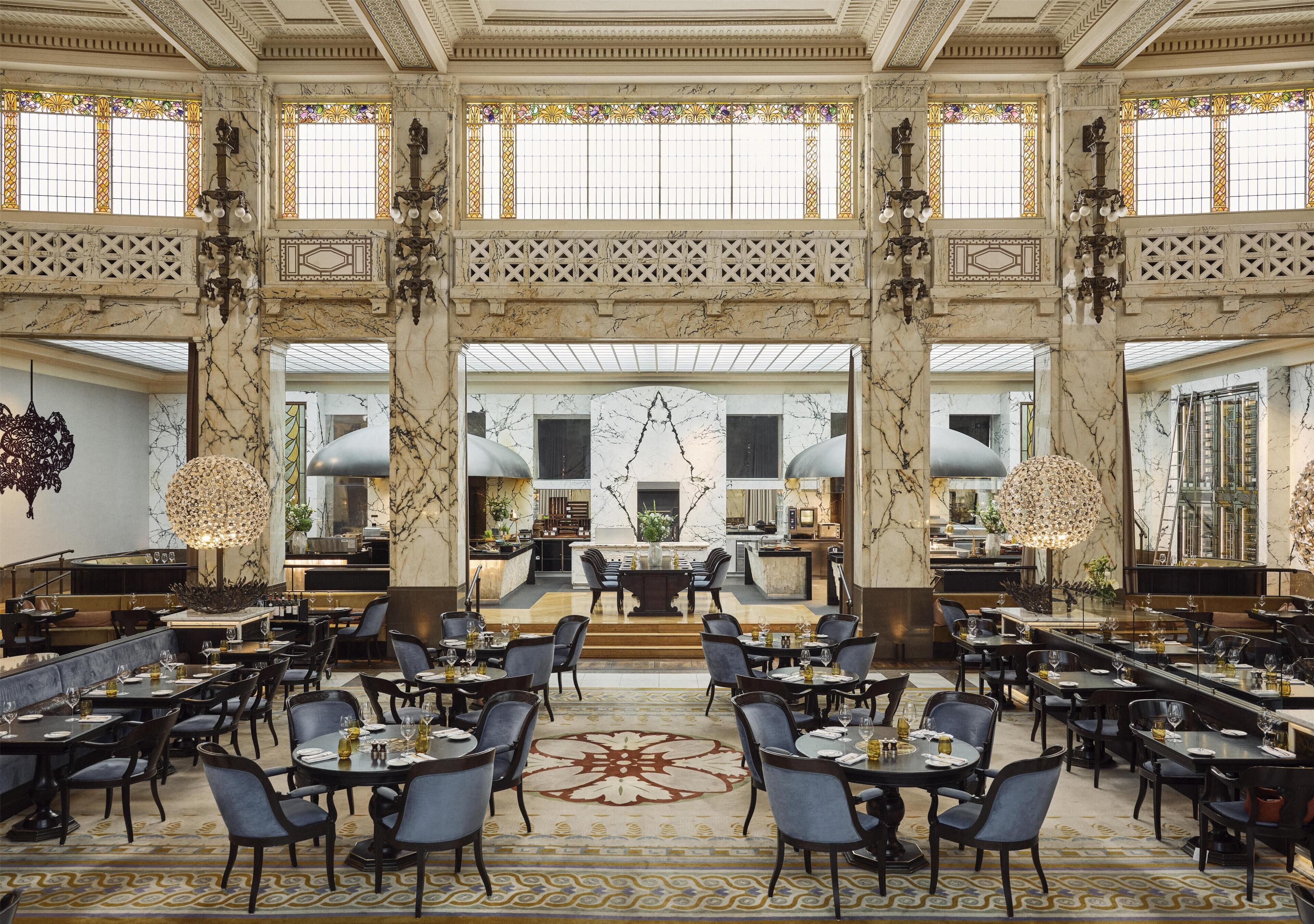 A spacious dining area with marble columns, large windows, and a central chandelier.