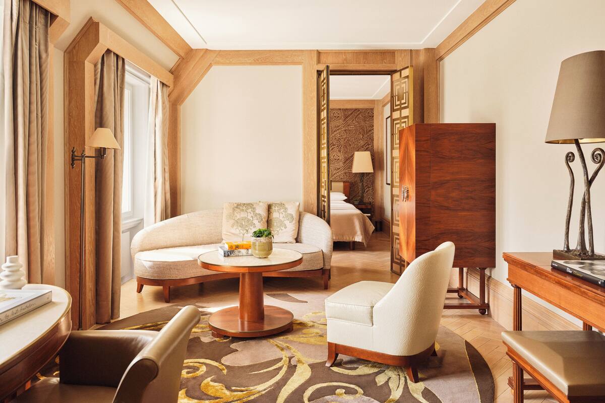 Een hotelkamer met een bank, fauteuil, een rond bijzettafeltje en een bed met hoofdeinde.