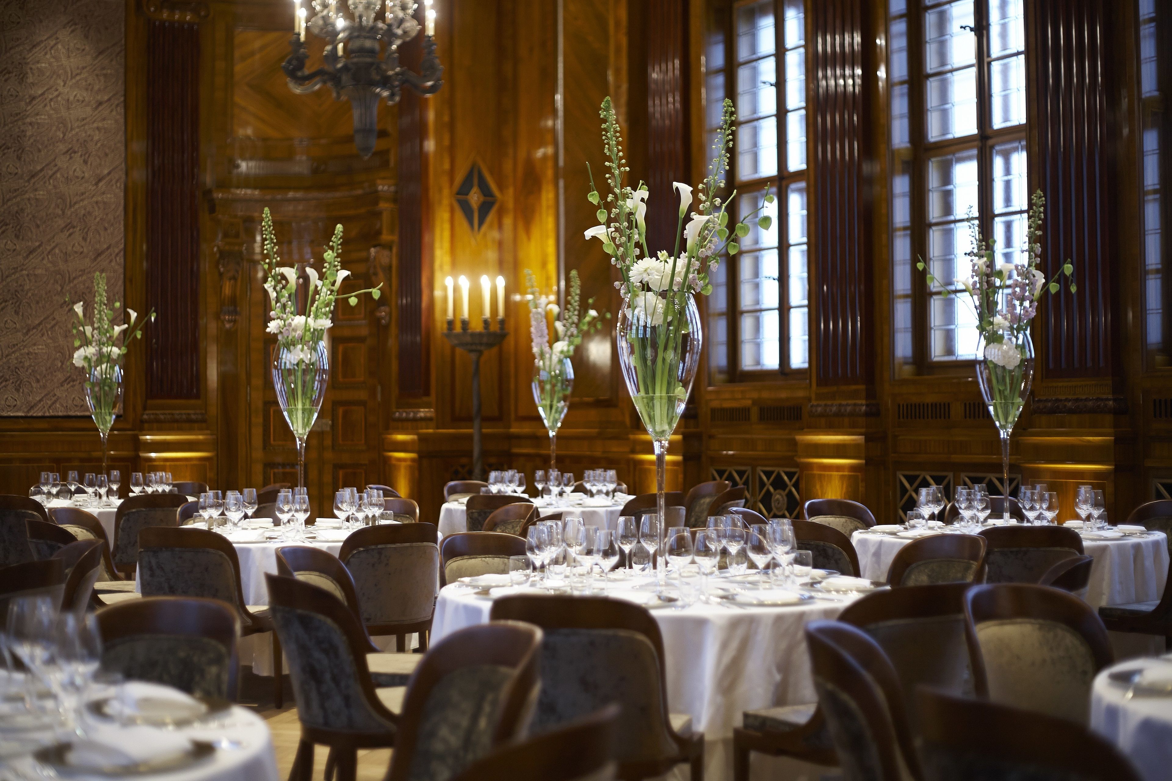 A formal dining room with round tables, chairs, and floral centerpieces.