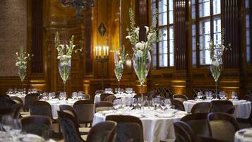 A formal dining room with round tables, chairs, and floral centerpieces.