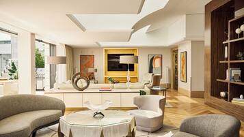 A spacious living room with a sofa, armchairs, a glass coffee table, and a wooden bookshelf.