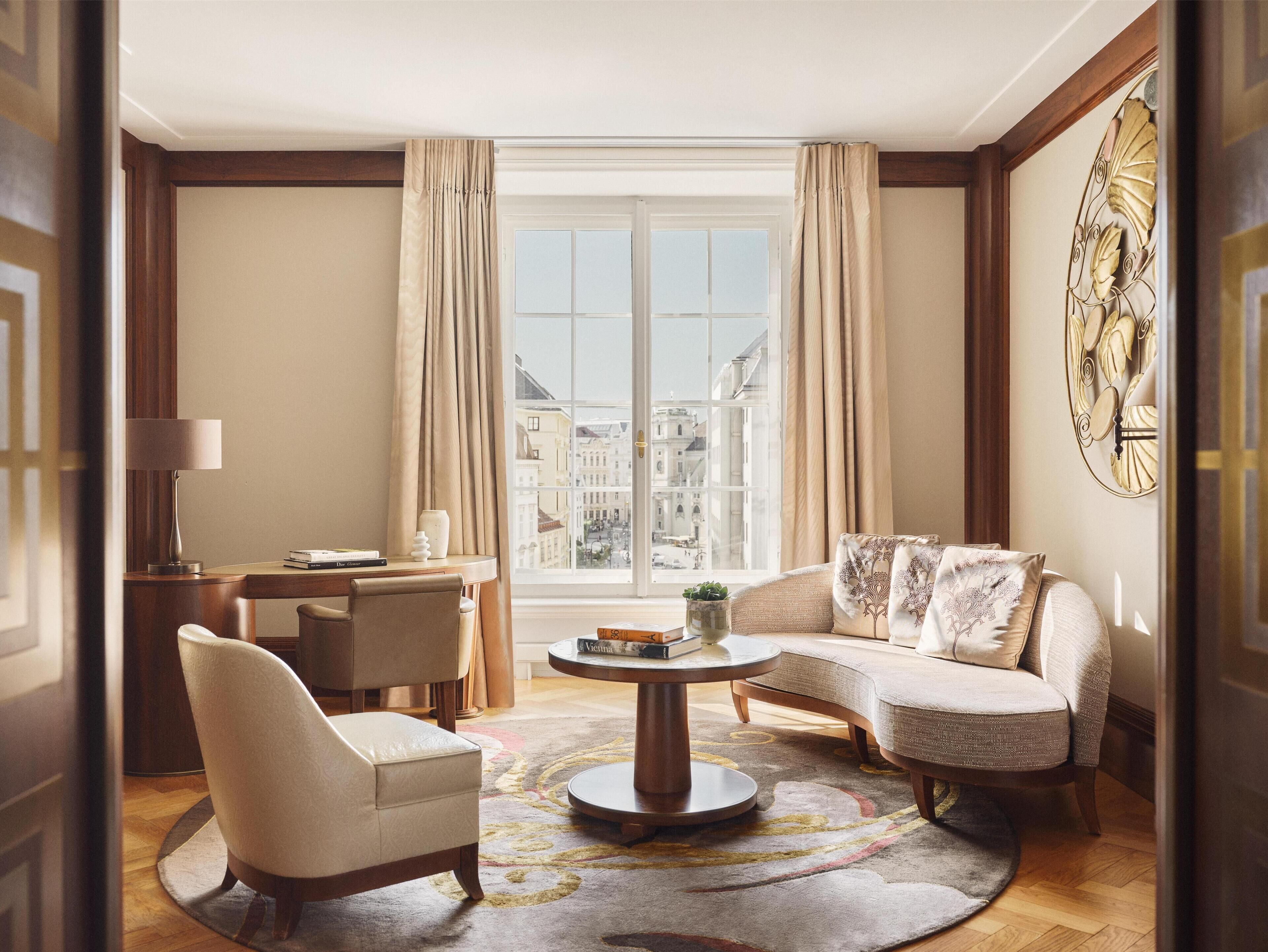 Uma sala de estar espaçosa com uma janela grande, uma mesa de centro redonda, um sofá e uma poltrona.