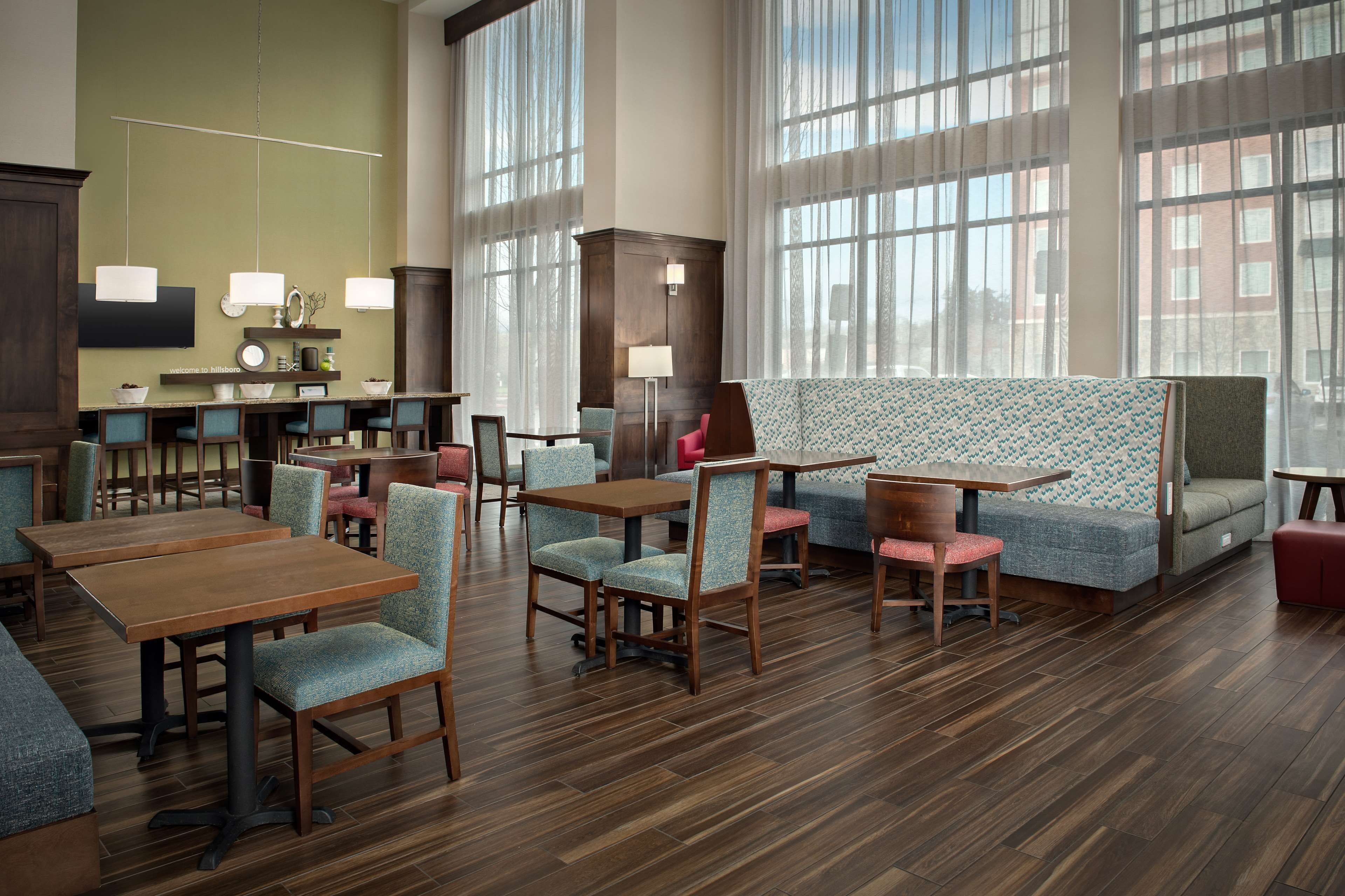 A spacious hotel lobby with multiple seating areas, including tables and chairs, and a large window providing natural light.