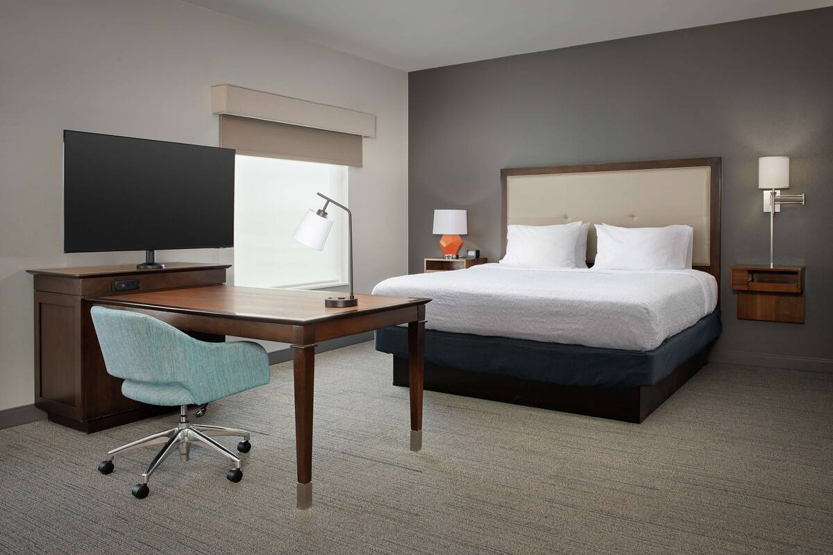 A hotel room with a large bed, a desk with a chair, a television, and a lamp.