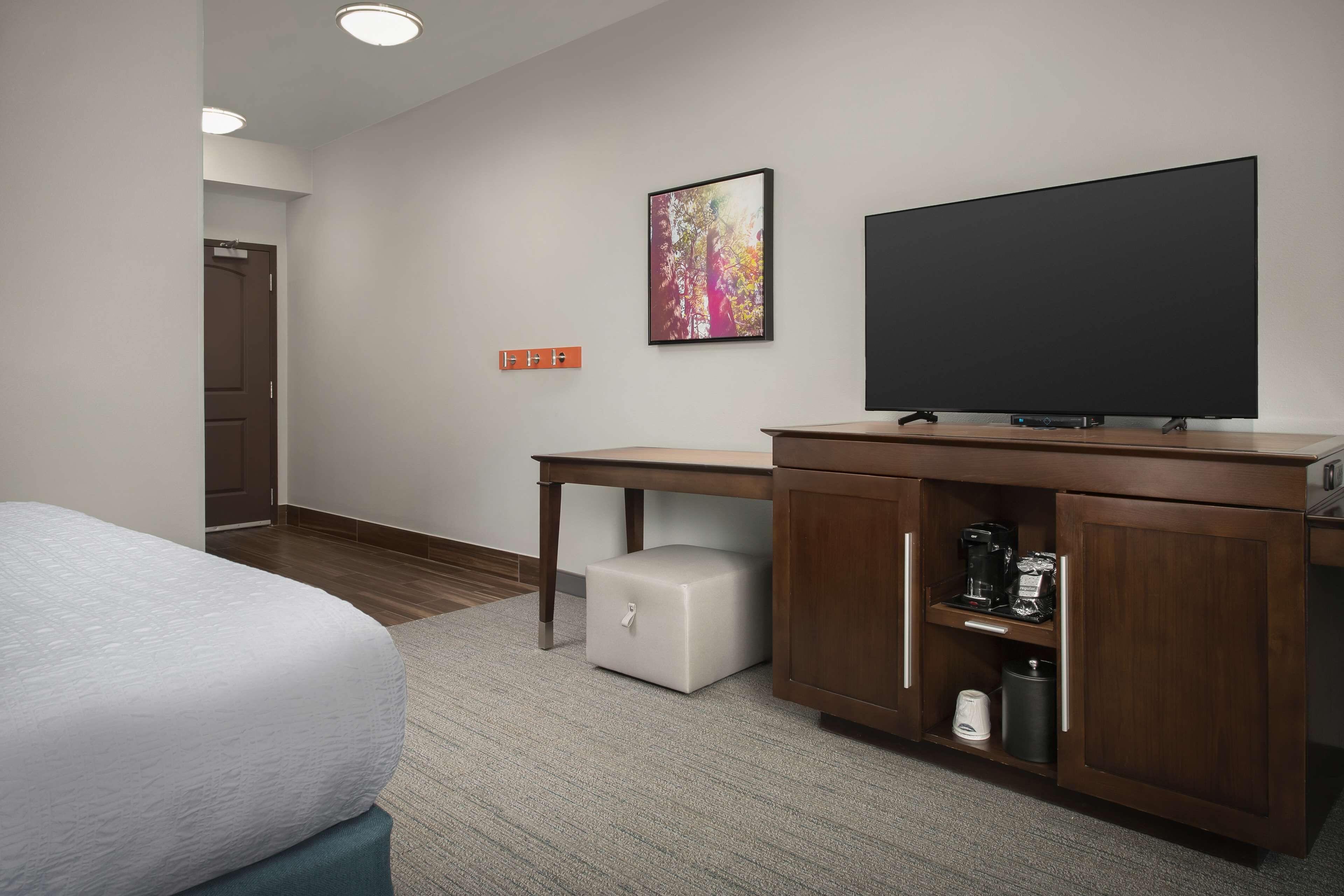 A hotel room with a bed, a desk, a television, a coffee maker, and a trash can.