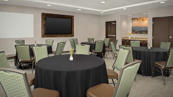 A conference room with round tables and chairs, a large screen, and a painting of a sunset.