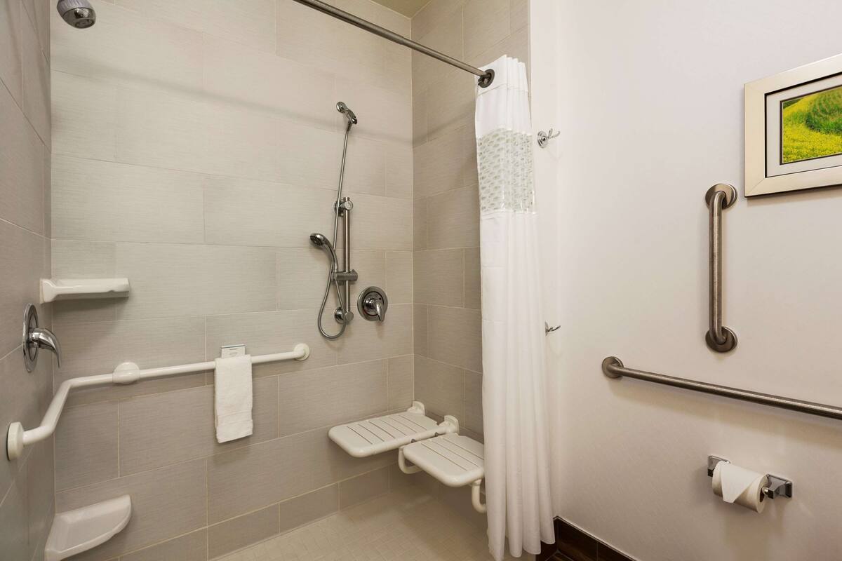 A bathroom with a shower, grab bars, a toilet, and a towel rack.