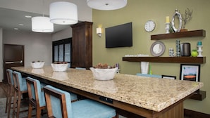 A kitchen with a granite countertop, wooden chairs, and a TV mounted on the wall.