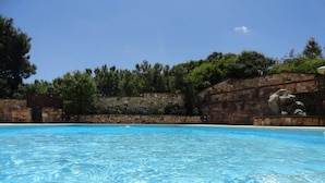 Piscina azul translúcida cercada por muros de pedra e árvores.