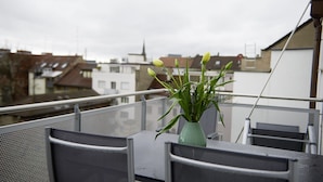 A balcony with a table and chairs, a green vase with plants, and a view of buildings in the background. - Residence Apartments by Hotel du Commerce (Basel)