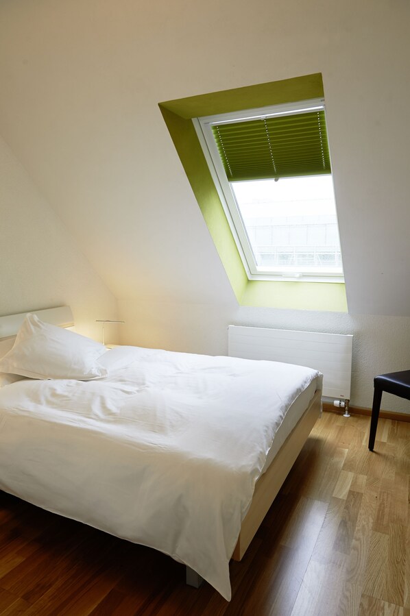 A bedroom with a bed, a nightstand, a window with blinds, and a radiator.