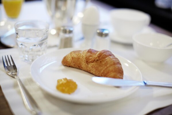 A breakfast setting with a croissant, butter, a fork, a knife, a glass of water, and salt and pepper shakers on a table.