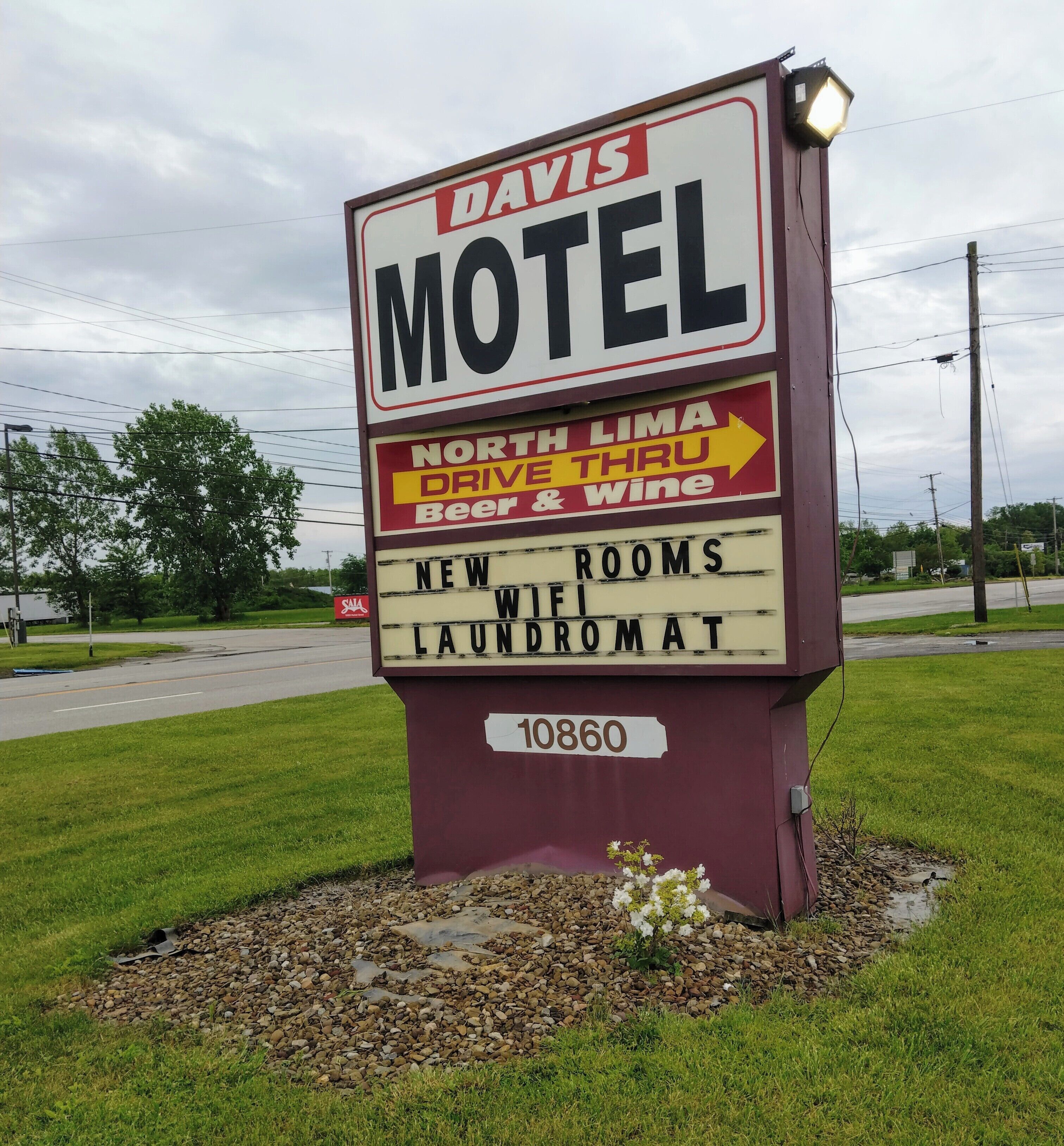 Een motelteken met de tekst 'DAVIS MOTEL' en 'NORTH LIMA DRIVE THRU Bier & Wijn'. Er staat 'NEW WOLF ROOMS LAUNDROMAT' op, en het getal '10860' is zichtbaar.