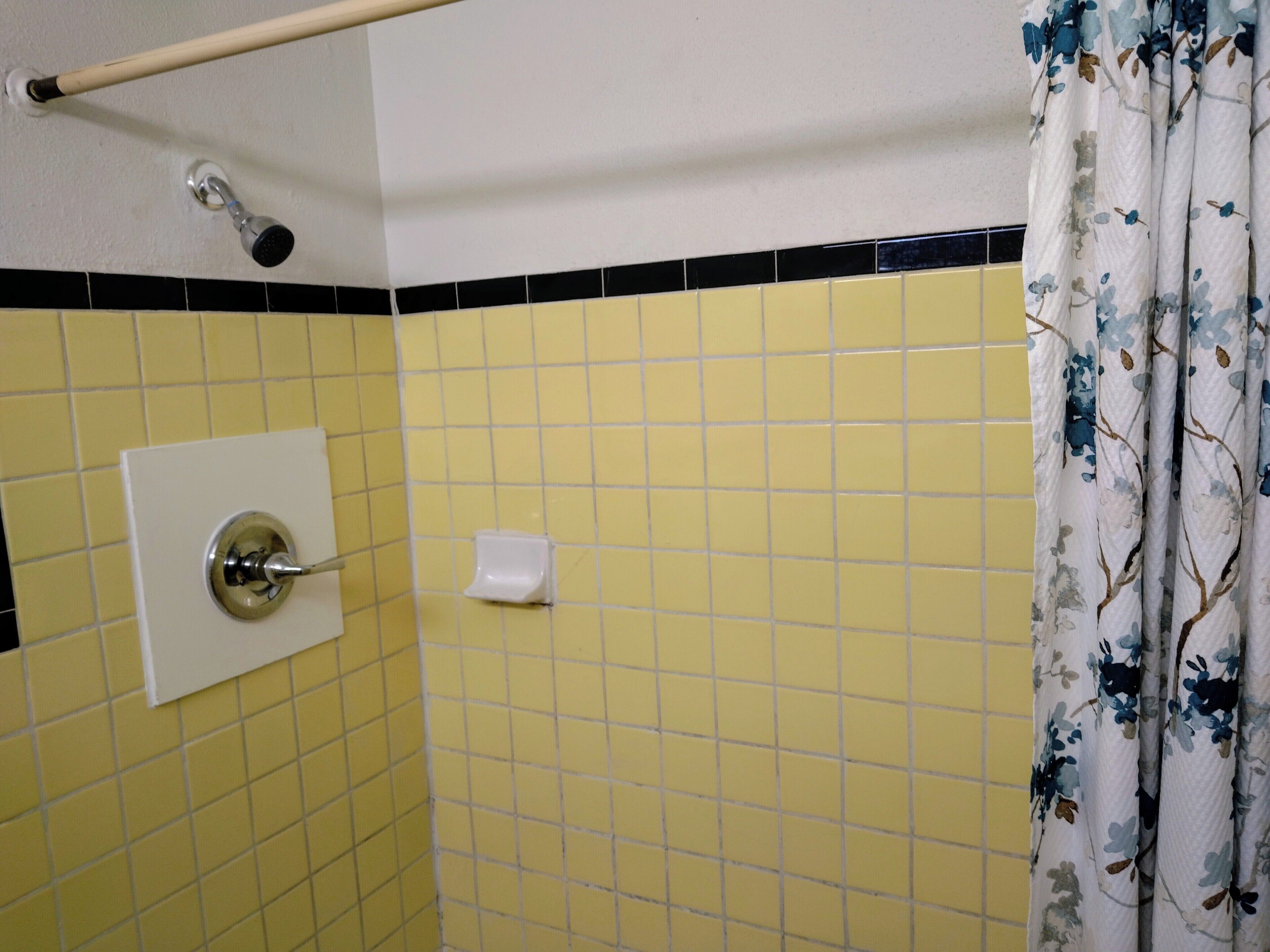 A bathroom with yellow and black tiled walls, a white toilet, a hand dryer, and a shower curtain with a floral pattern.
