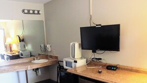 Habitación de hotel con mostrador de madera, lavabo, microondas, secador de pelo, televisor y una silla.