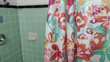 A bathroom with green tiles, a shower curtain with a floral pattern, and a visible showerhead.