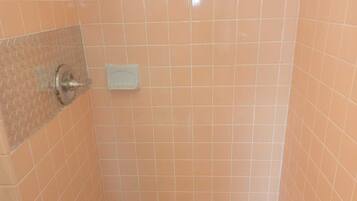 Zona de ducha con azulejos, cabezal de ducha manual y jabonera.