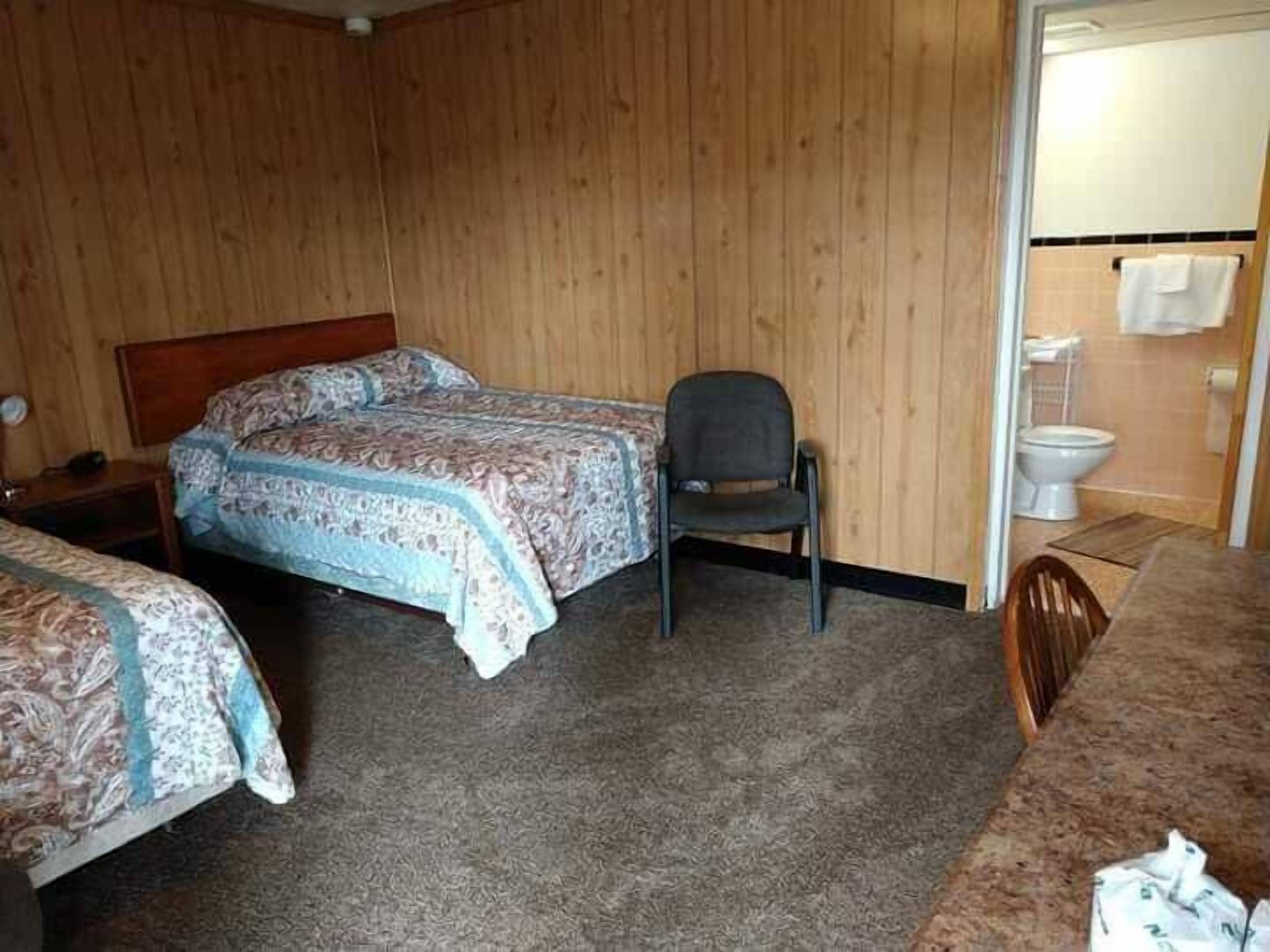 Une chambre avec deux lits, une chaise, une petite table et des toilettes.